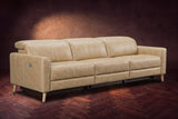 The Elodie sofa on a dark walnut herringbone floor against a plaster wall, three-quarter view, headrests down and footrests closed. Shown in Washed Sand, 3 seat.