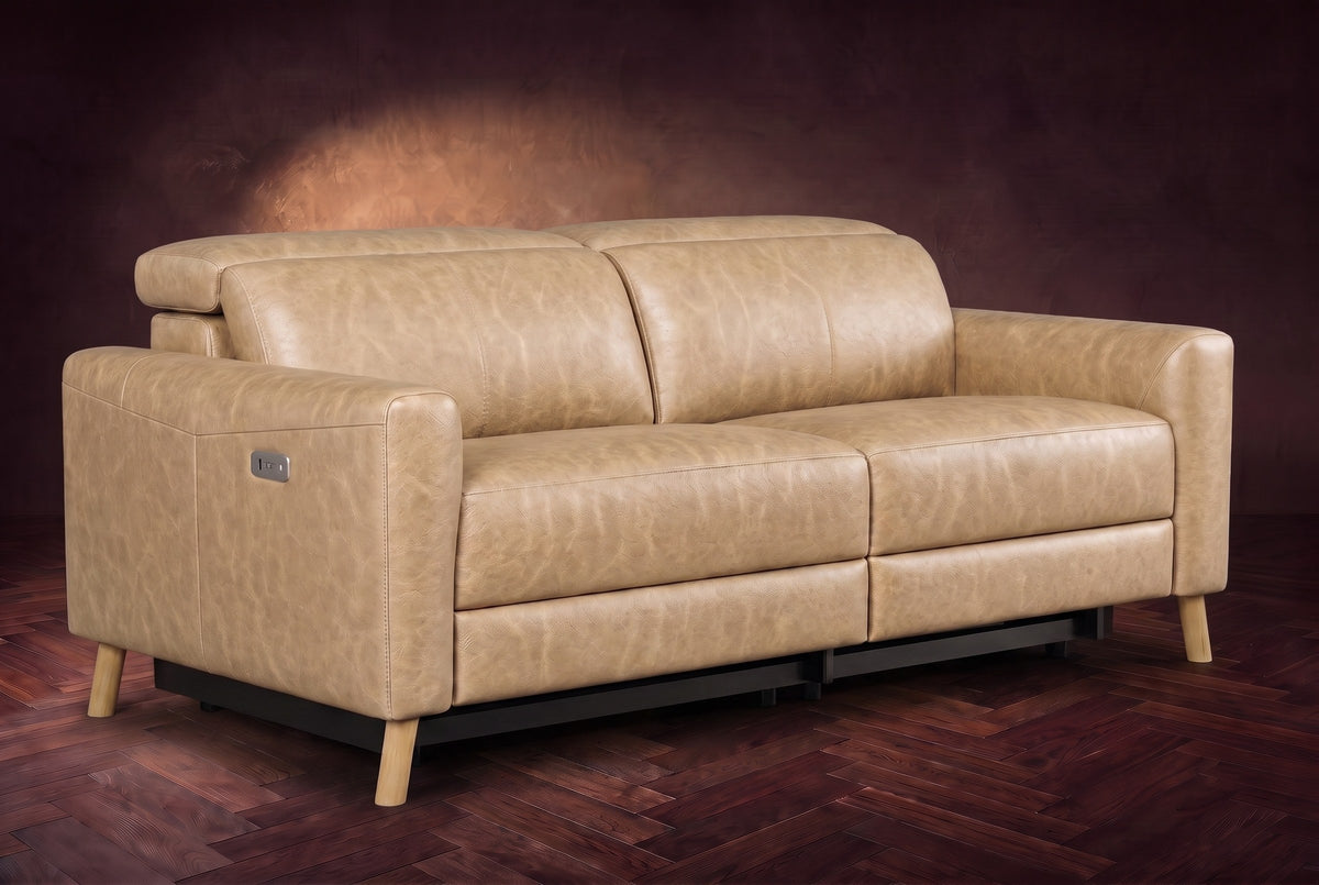 The Elodie loveseat on a dark walnut herringbone floor against a plaster wall, three-quarter view, headrests down and footrests closed. Shown in Washed Sand, Loveseat.