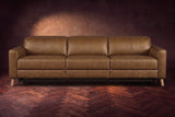 The Elodie sofa seen from the front on a dark walnut herringbone floor against a plaster wall, headrests down and footrests closed. Shown in Weathered Saddle, 3 seat.