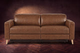 The Elodie loveseat seen from the front on a dark walnut herringbone floor against a plaster wall, headrests down and footrests closed. Shown in Weathered Saddle, Loveseat.