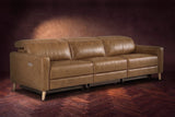 The Elodie sofa on a dark walnut herringbone floor against a plaster wall, three-quarter view, headrests down and footrests closed. Shown in Weathered Saddle, 3 seat.