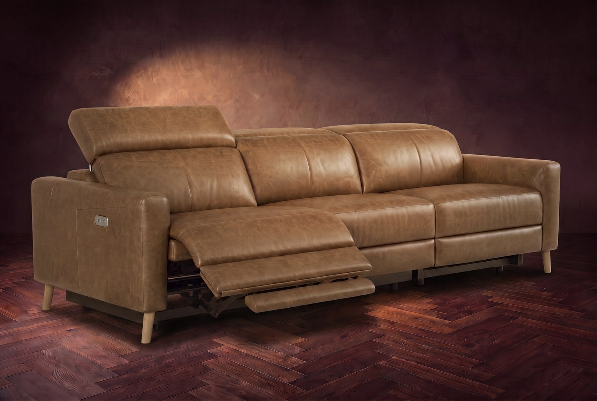 The Elodie sofa on a dark walnut herringbone floor, the left outer seat reclined with its footrest out and its headrest raised. Shown in Weathered Saddle, 3 seat.