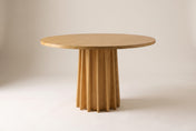 Elowen oak round pedestal dining table in Natural Oak, three-quarter view on a warm off-white studio backdrop