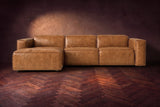 The Emery sectional in Antiqued Caramel distressed leather seen from the front on a dark walnut herringbone floor, headrests down and footrest closed. Shown in Antiqued Caramel, Left chaise.