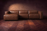 The Emery sectional in Burnished Chestnut distressed leather seen from the front on a dark walnut herringbone floor, headrests down and footrest closed. Shown in Burnished Chestnut, Left chaise.