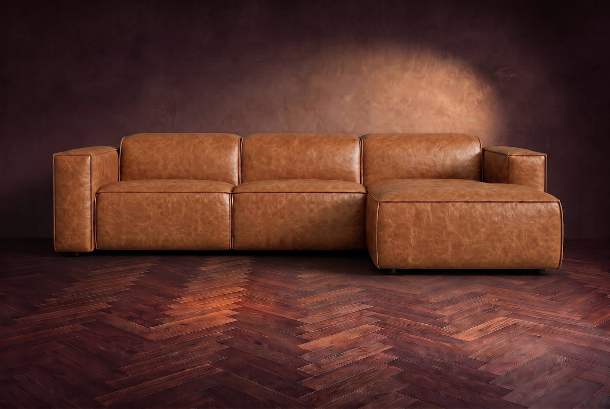 The Emery sectional in Tuscan Cognac distressed leather seen from the front on a dark walnut herringbone floor, headrests down and footrest closed. Shown in Tuscan Cognac, Right chaise.