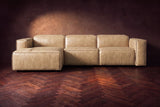 The Emery sectional in Washed Sand distressed leather seen from the front on a dark walnut herringbone floor, headrests down and footrest closed. Shown in Washed Sand, Left chaise.