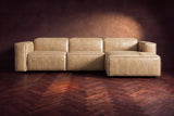 The Emery sectional in Washed Sand distressed leather seen from the front on a dark walnut herringbone floor, headrests down and footrest closed. Shown in Washed Sand, Right chaise.