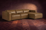 The Emery sectional in Weathered Saddle distressed leather on a dark walnut herringbone floor against a warm plaster wall, three-quarter view, headrests down and footrest closed. Shown in Weathered Saddle, Right chaise.