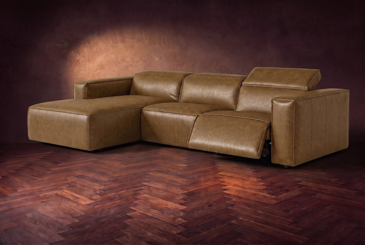 The Emery sectional in Weathered Saddle distressed leather on a dark walnut herringbone floor, the arm-end recliner open: its one-piece footrest out and its headrest raised. Shown in Weathered Saddle, Left chaise.