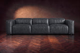 The Emery 3 seat seen from the front in Aged Slate distressed full leather on a dark herringbone floor, headrests down. Shown in Aged Slate, 3 seat.