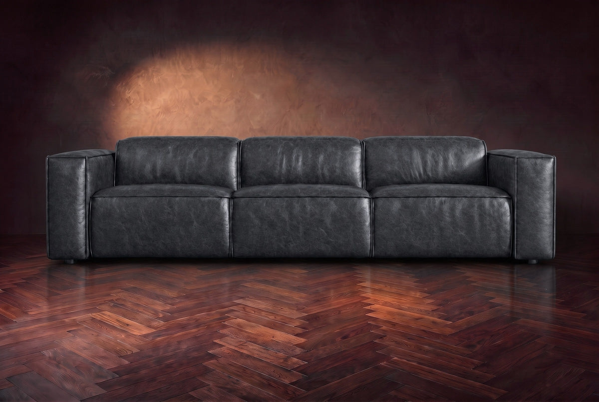 The Emery 3 seat seen from the front in Aged Slate distressed full leather on a dark herringbone floor, headrests down. Shown in Aged Slate, 3 seat.