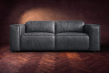 The Emery loveseat seen from the front in Aged Slate distressed full leather on a dark herringbone floor, headrests down. Shown in Aged Slate, Loveseat.