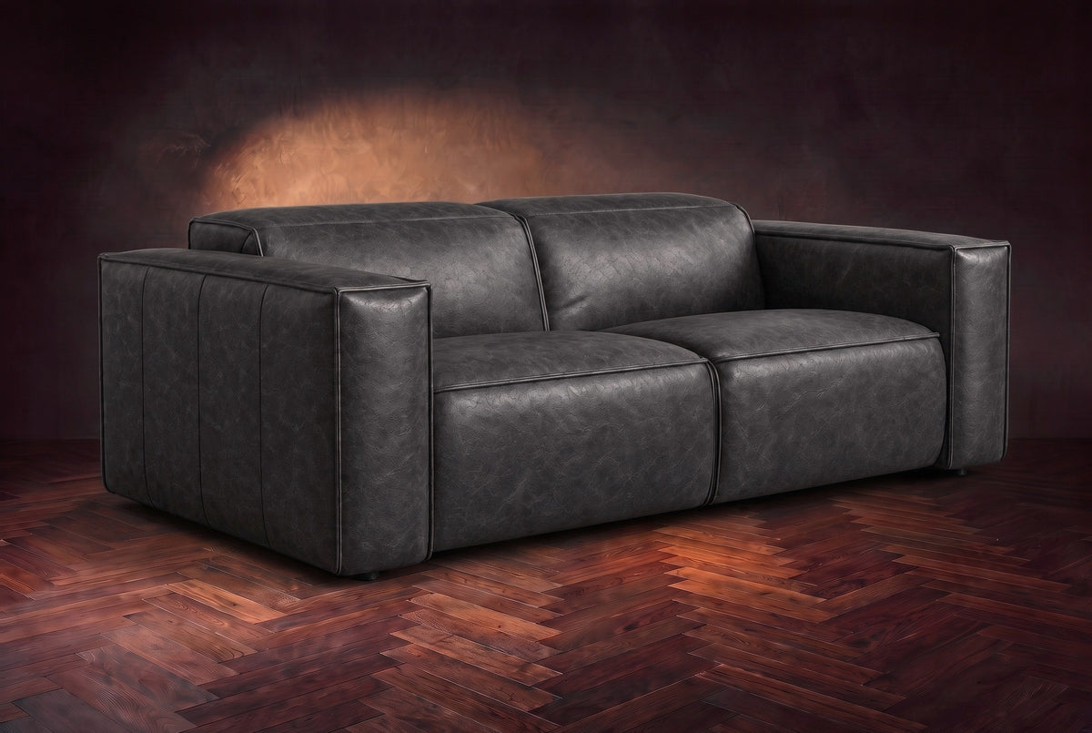 The Emery loveseat in Aged Slate distressed full leather on a dark herringbone floor, headrests down and footrests closed. Shown in Aged Slate, Loveseat.