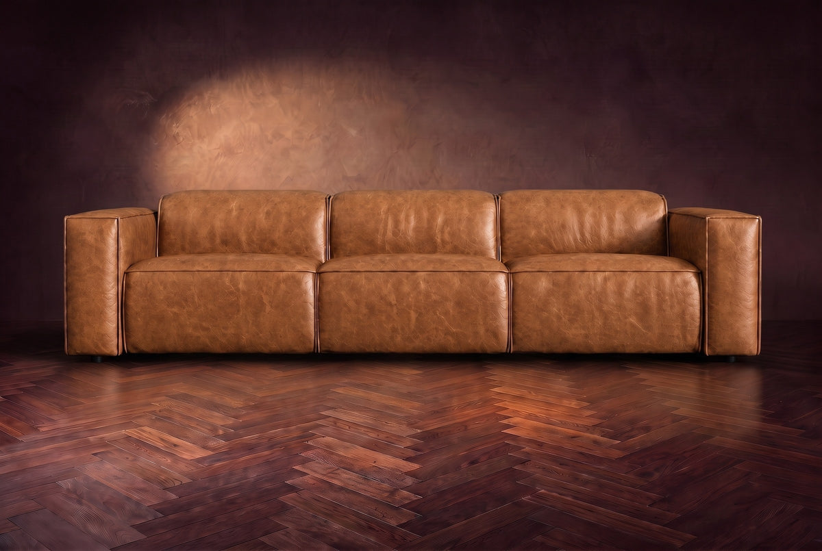The Emery 3 seat seen from the front in Antiqued Caramel distressed full leather on a dark herringbone floor, headrests down. Shown in Antiqued Caramel, 3 seat.