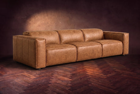 The Emery 3 seat in Antiqued Caramel distressed full leather on a dark herringbone floor, headrests down and footrests closed. Shown in Antiqued Caramel, 3 seat.
