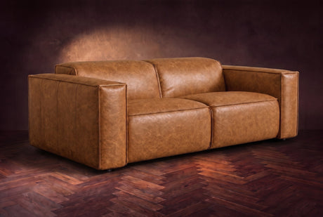 The Emery loveseat in Antiqued Caramel distressed full leather on a dark herringbone floor, headrests down and footrests closed. Shown in Antiqued Caramel, Loveseat.