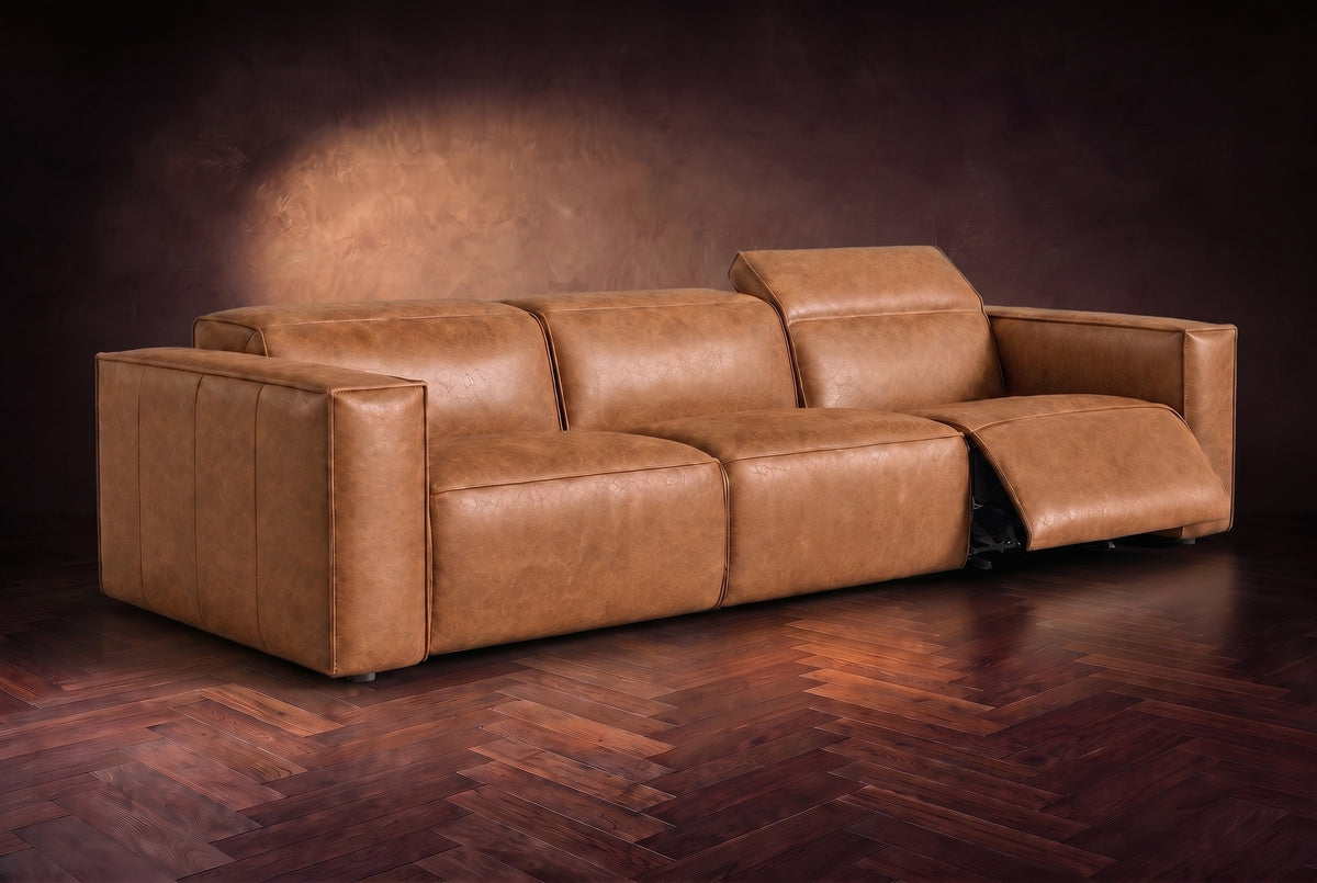 The Emery 3 seat in Antiqued Caramel on a dark herringbone floor, the right-hand recliner open with its one-piece footrest out and its headrest raised. Shown in Antiqued Caramel, 3 seat.