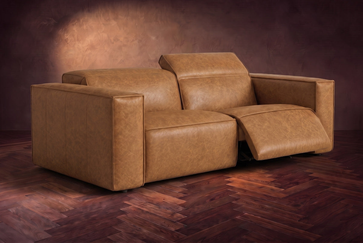 The Emery loveseat in Antiqued Caramel on a dark herringbone floor, the right-hand recliner open with its one-piece footrest out and its headrest raised. Shown in Antiqued Caramel, Loveseat.