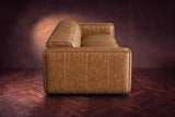 The panelled box arm of the Emery sofa seen from the side in Antiqued Caramel, on a dark herringbone floor. Shown in Antiqued Caramel, 3 seat.
