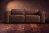 The Emery loveseat seen from the front in Burnished Chestnut distressed full leather on a dark herringbone floor, headrests down. Shown in Burnished Chestnut, Loveseat.