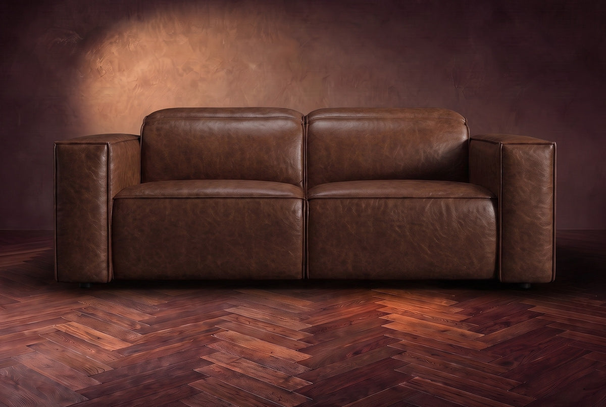 The Emery loveseat seen from the front in Burnished Chestnut distressed full leather on a dark herringbone floor, headrests down. Shown in Burnished Chestnut, Loveseat.