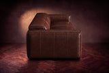 The panelled box arm of the Emery sofa seen from the side in Burnished Chestnut, on a dark herringbone floor. Shown in Burnished Chestnut, 3 seat.