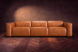The Emery 3 seat seen from the front in Tuscan Cognac distressed full leather on a dark herringbone floor, headrests down. Shown in Tuscan Cognac, 3 seat.