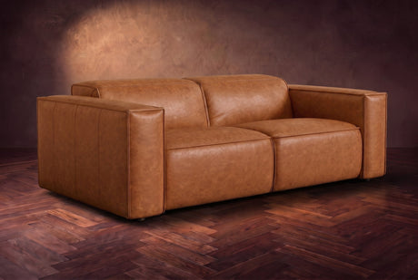 The Emery loveseat in Tuscan Cognac distressed full leather on a dark herringbone floor, headrests down and footrests closed. Shown in Tuscan Cognac, Loveseat.