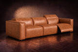 The Emery 3 seat in Tuscan Cognac on a dark herringbone floor, the right-hand recliner open with its one-piece footrest out and its headrest raised. Shown in Tuscan Cognac, 3 seat.