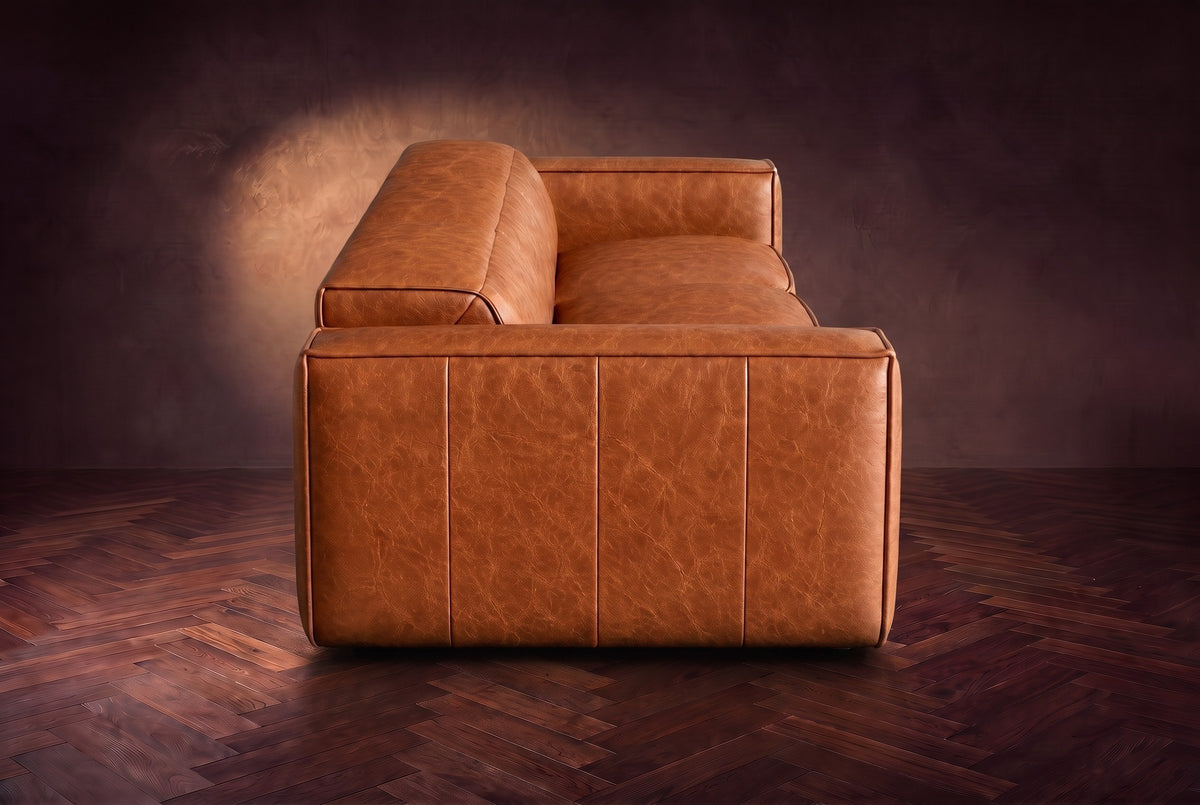 The panelled box arm of the Emery sofa seen from the side in Tuscan Cognac, on a dark herringbone floor. Shown in Tuscan Cognac, 3 seat.
