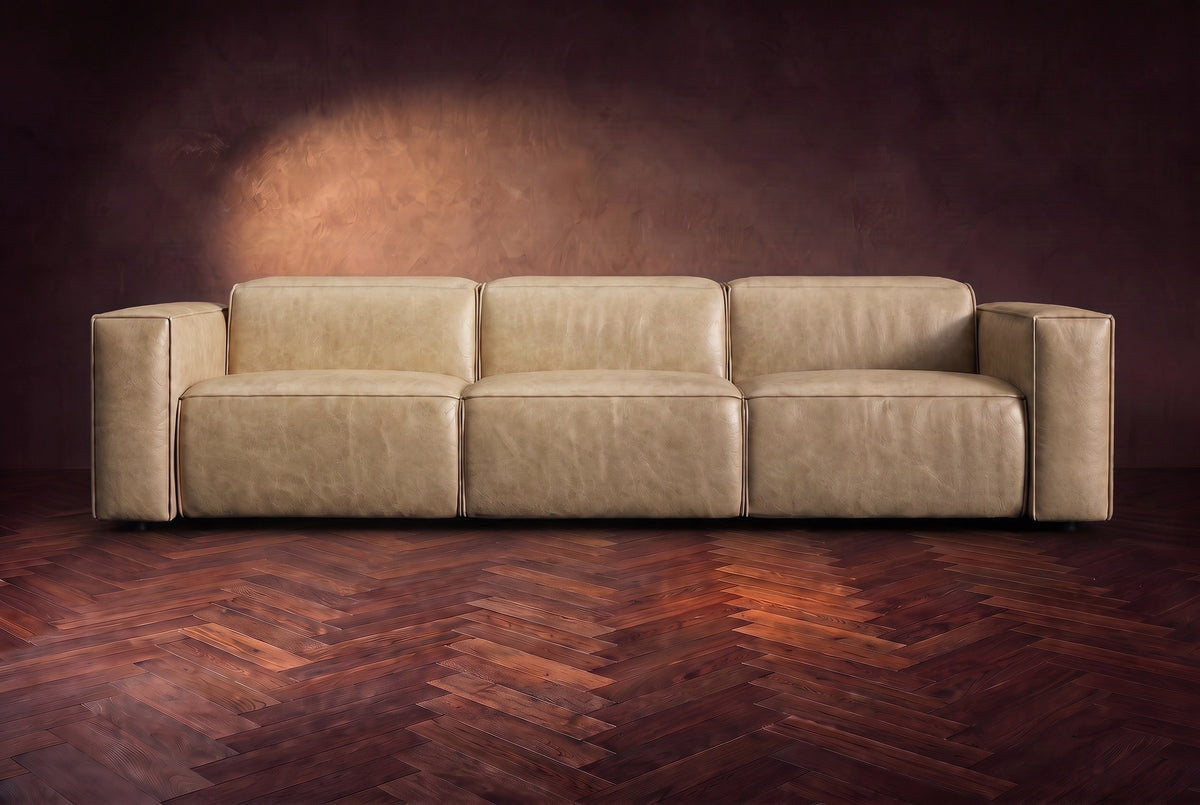 The Emery 3 seat seen from the front in Washed Sand distressed full leather on a dark herringbone floor, headrests down. Shown in Washed Sand, 3 seat.