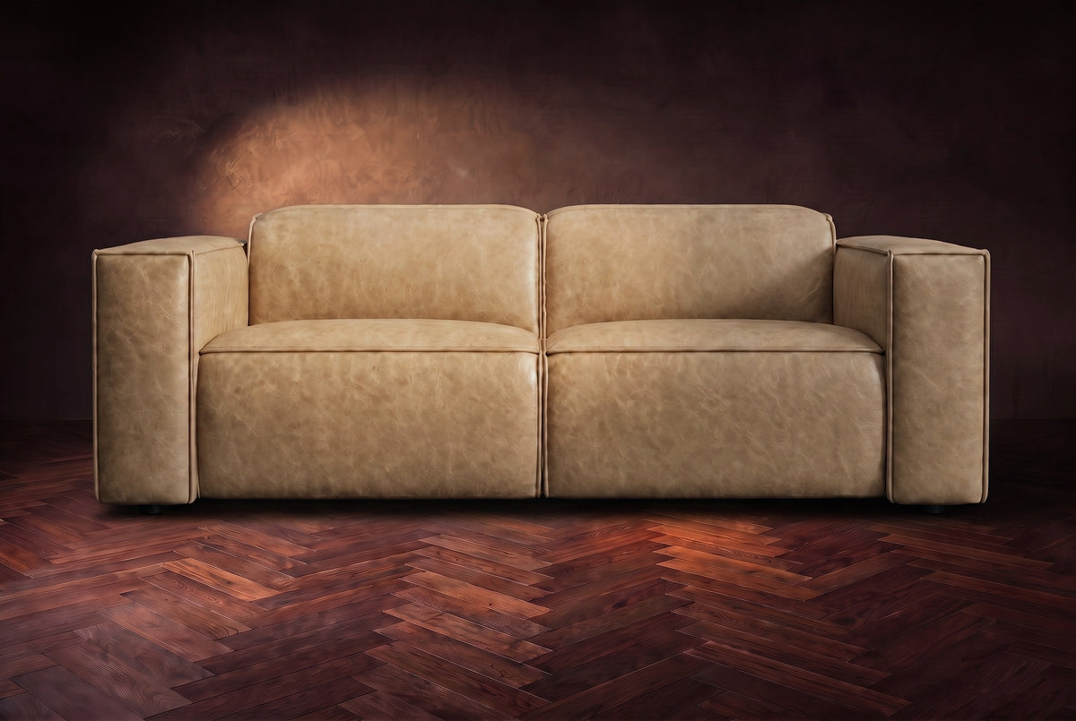The Emery loveseat seen from the front in Washed Sand distressed full leather on a dark herringbone floor, headrests down. Shown in Washed Sand, Loveseat.