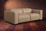 The Emery loveseat in Washed Sand distressed full leather on a dark herringbone floor, headrests down and footrests closed. Shown in Washed Sand, Loveseat.