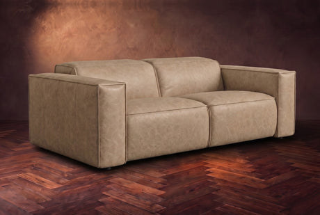 The Emery loveseat in Washed Sand distressed full leather on a dark herringbone floor, headrests down and footrests closed. Shown in Washed Sand, Loveseat.