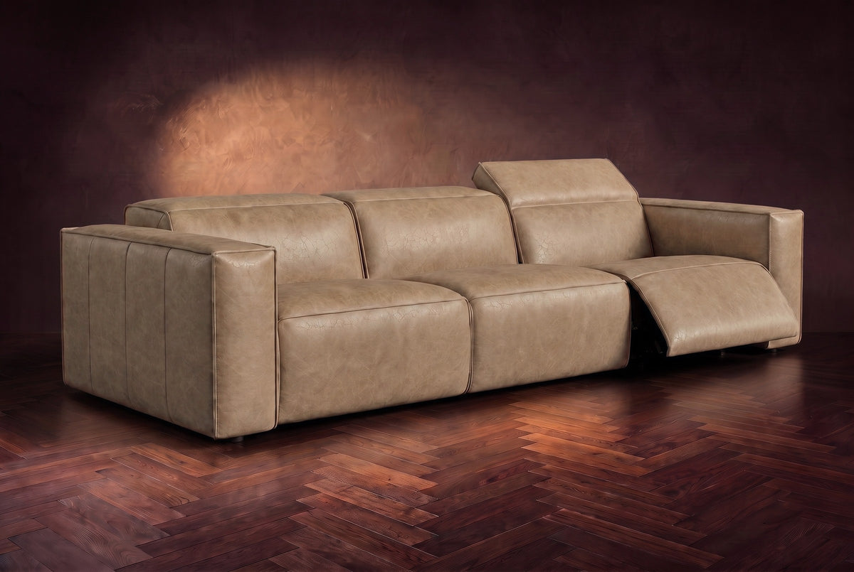 The Emery 3 seat in Washed Sand on a dark herringbone floor, the right-hand recliner open with its one-piece footrest out and its headrest raised. Shown in Washed Sand, 3 seat.