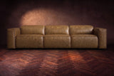The Emery 3 seat seen from the front in Weathered Saddle distressed full leather on a dark herringbone floor, headrests down. Shown in Weathered Saddle, 3 seat.