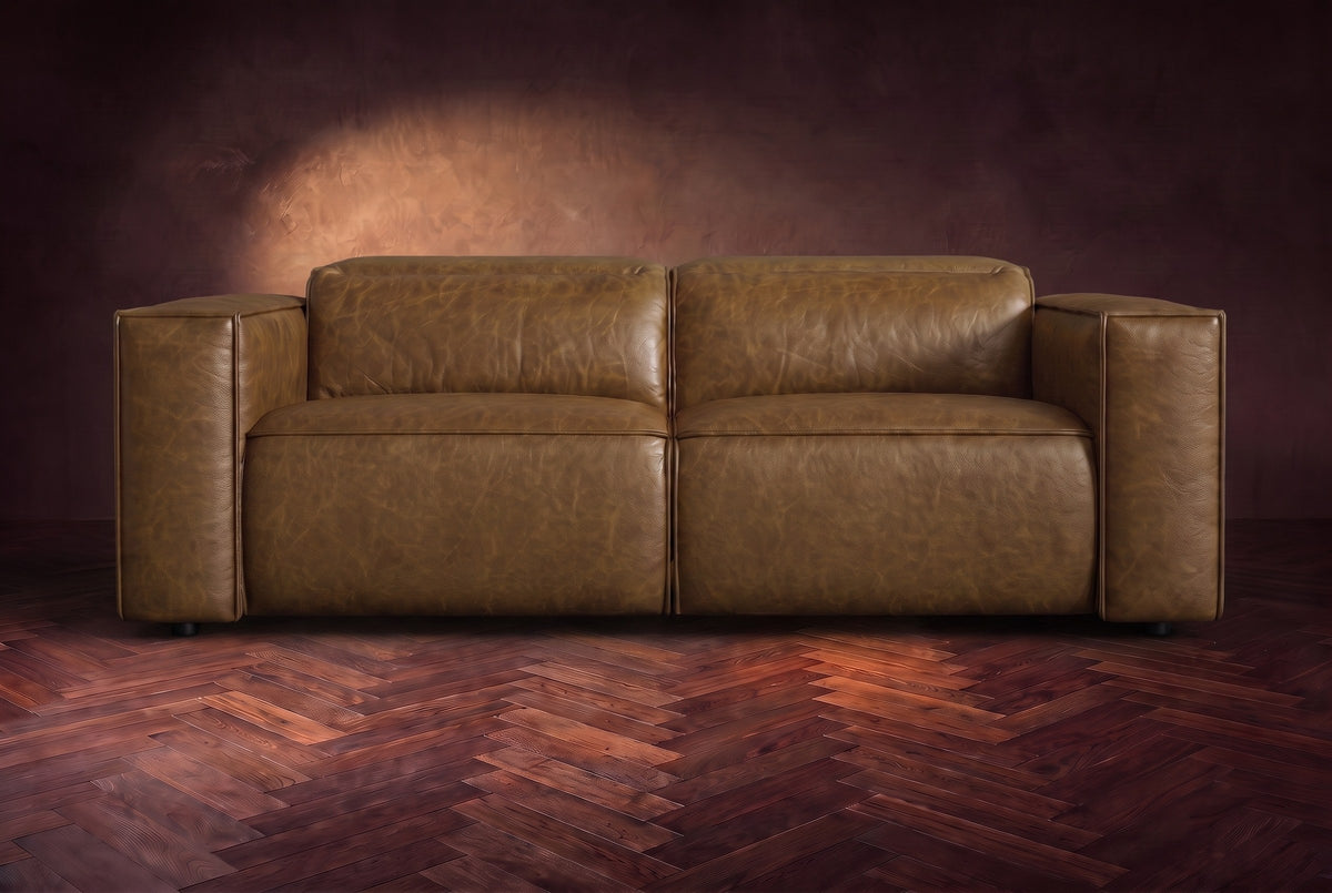 The Emery loveseat seen from the front in Weathered Saddle distressed full leather on a dark herringbone floor, headrests down. Shown in Weathered Saddle, Loveseat.