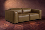 The Emery loveseat in Weathered Saddle distressed full leather on a dark herringbone floor, headrests down and footrests closed. Shown in Weathered Saddle, Loveseat.
