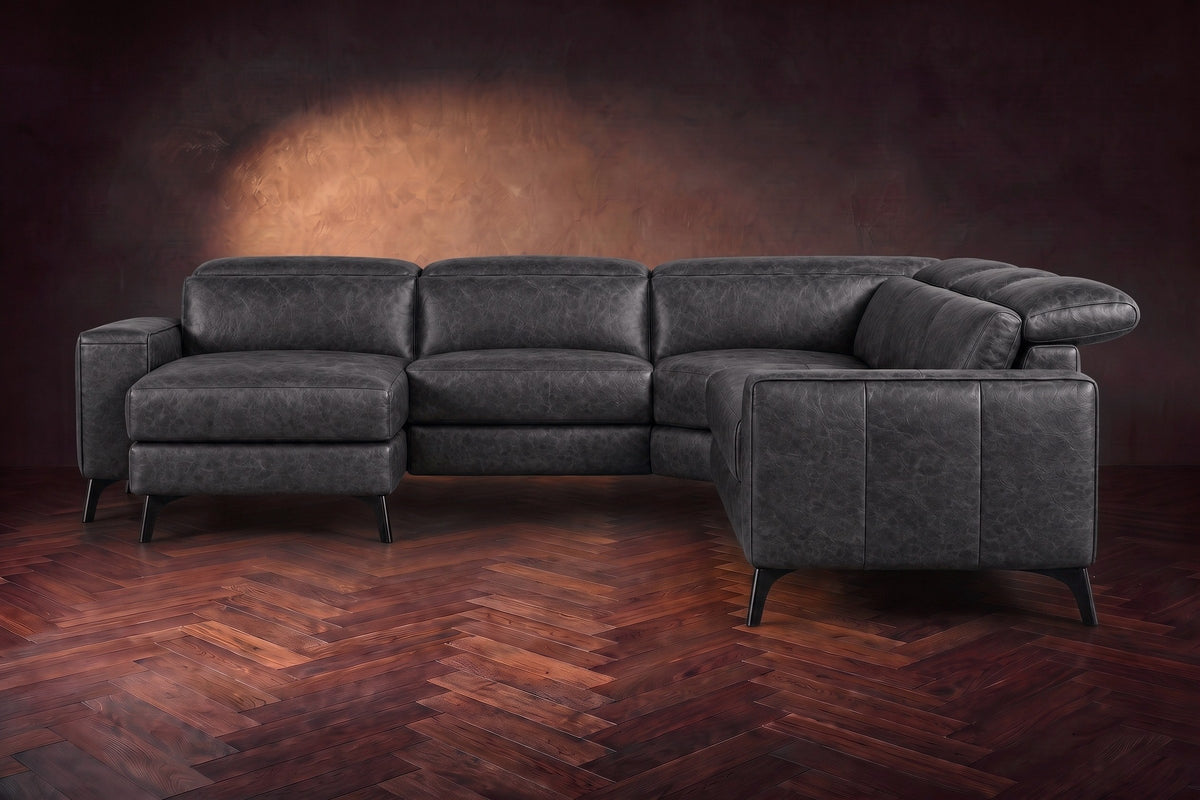 The Esther sectional seen from the front in Aged Slate distressed full leather on a dark herringbone floor, the chaise facing the camera and the footrest closed. Shown in Aged Slate, Left chaise.