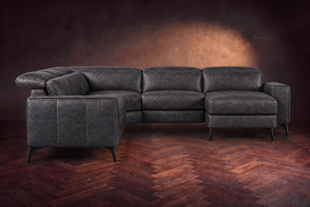 The Esther sectional seen from the front in Aged Slate distressed full leather on a dark herringbone floor, the chaise facing the camera and the footrest closed. Shown in Aged Slate, Right chaise.
