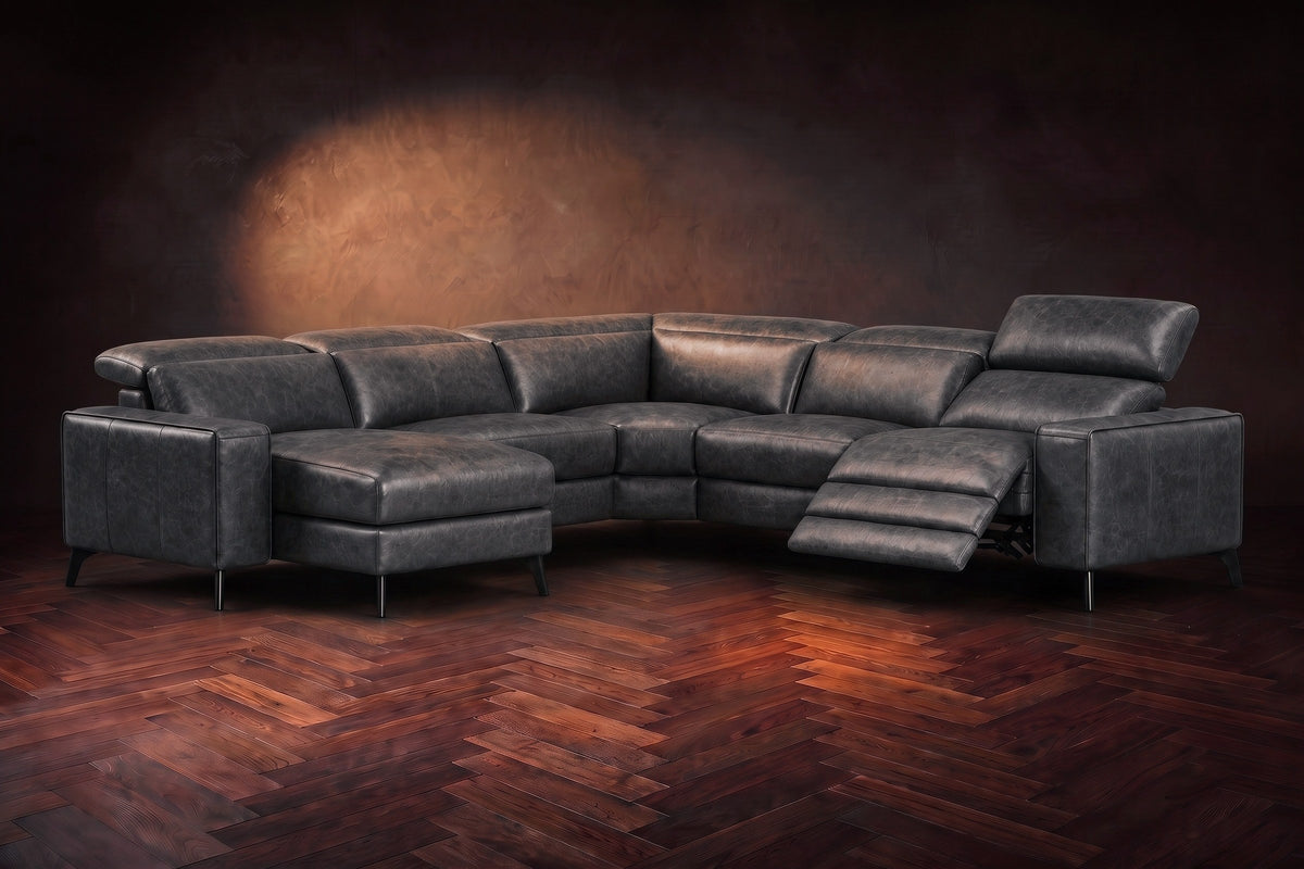 The Esther sectional in Aged Slate distressed full leather on a dark herringbone floor, the power recliner at the arm end open with its one-piece footrest out and its headrest raised. Shown in Aged Slate, Left chaise.