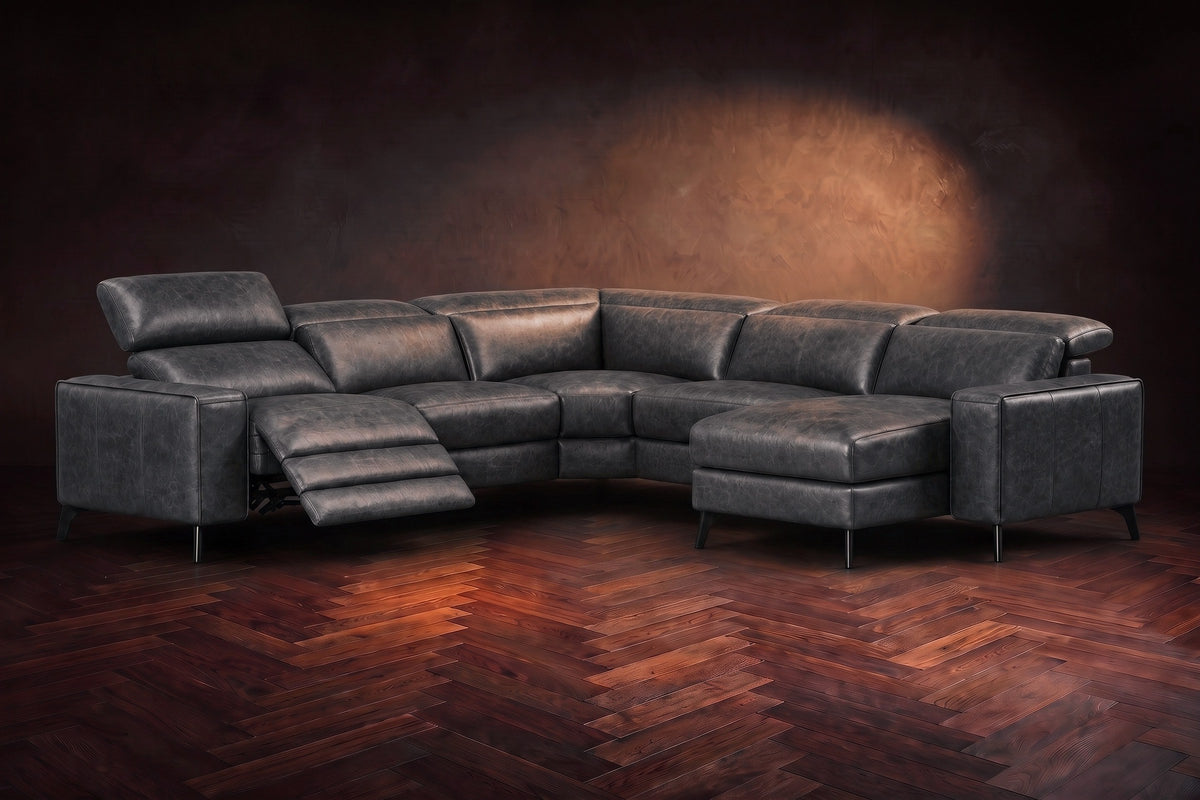 The Esther sectional in Aged Slate distressed full leather on a dark herringbone floor, the power recliner at the arm end open with its one-piece footrest out and its headrest raised. Shown in Aged Slate, Right chaise.