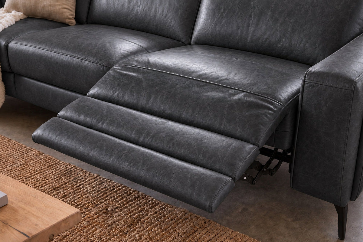 The open Esther recliner in Aged Slate beside its box arm, the one-piece footrest out over a jute rug, a cushion and a knit throw on the next seat. Shown in Aged Slate, Left chaise.