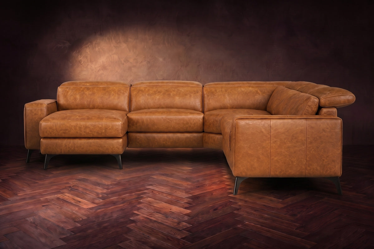 The Esther sectional seen from the front in Antiqued Caramel distressed full leather on a dark herringbone floor, the chaise facing the camera and the footrest closed. Shown in Antiqued Caramel, Left chaise.