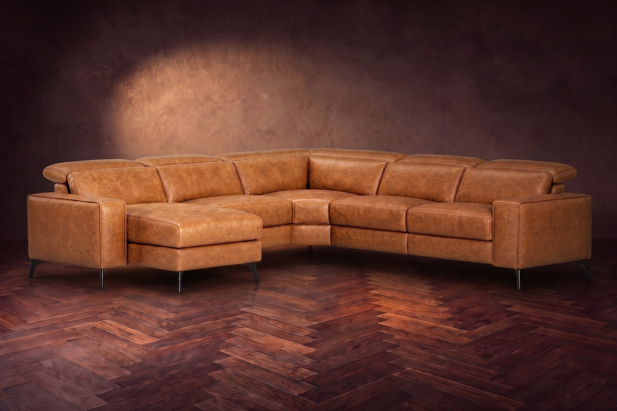 The Esther sectional in Antiqued Caramel distressed full leather on a dark herringbone floor, headrests down and footrest closed. Shown in Antiqued Caramel, Left chaise.