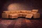 The Esther sectional in Antiqued Caramel distressed full leather on a dark herringbone floor, the power recliner at the arm end open with its one-piece footrest out and its headrest raised. Shown in Antiqued Caramel, Left chaise.