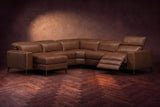 The Esther sectional in Burnished Chestnut distressed full leather on a dark herringbone floor, the power recliner at the arm end open with its one-piece footrest out and its headrest raised. Shown in Burnished Chestnut, Left chaise.