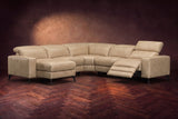 The Esther sectional in Washed Sand distressed full leather on a dark herringbone floor, the power recliner at the arm end open with its one-piece footrest out and its headrest raised. Shown in Washed Sand, Left chaise.