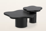 Exilles cloud-shaped coffee tables in black, set of two: a large low table and a smaller, taller one on round drum bases, on a warm white studio backdrop